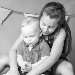 Older sibling holding baby’s hand in studio during cake smash family photos