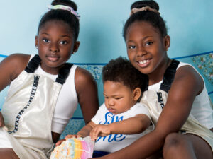 Siblings holding baby close during the cake smash, natural connection portrait
