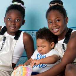 Siblings holding baby close during the cake smash, natural connection portrait