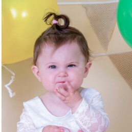 Baby smashing cake on studio set while parent laughs nearby, first birthday cake smash