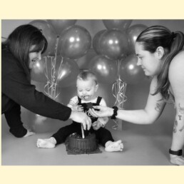 Grandparent cuddling baby in studio with parent nearby during first birthday photos