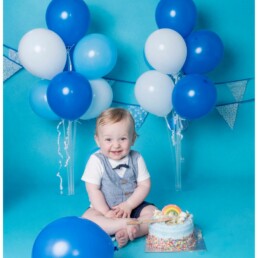 Close-up of baby’s determined expression with icing on hands during baby-led cake smash