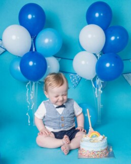 One-year-old sitting by cake in studio, taking time to explore during cake smash, West Sussex