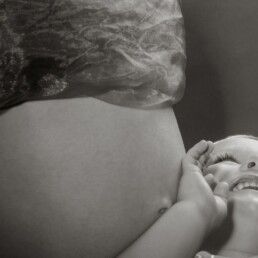 sibling with his unborn brothet cradled in his mohters arms
