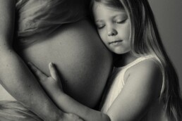 sibling with his unborn brothet cradled in his mohters arms