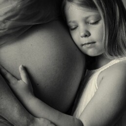 sibling with his unborn brothet cradled in his mohters arms